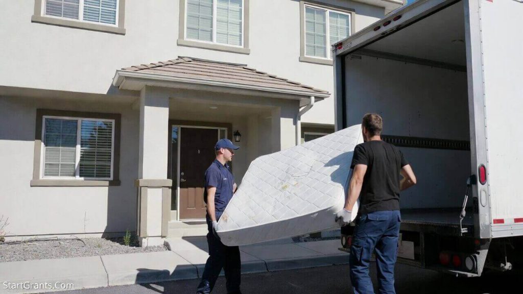 A delivery crew hauling away an old mattress through a retailer take-back program instead of donating it to a charity.