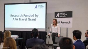 A mature female graduate student with a cane presenting her findings at a professional academic conference, funded by a specific travel grant.