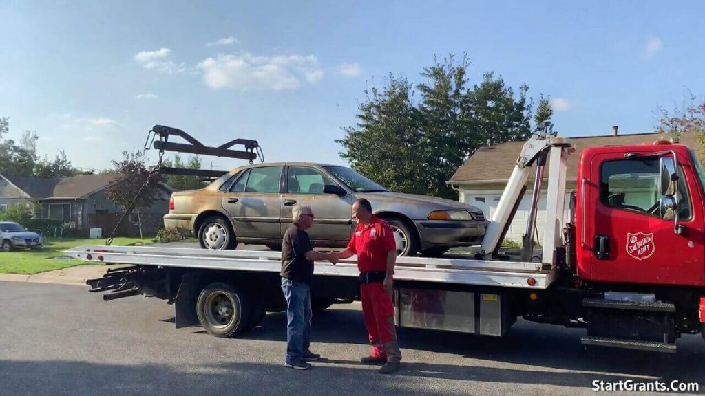A flatbed tow truck picking up a donated vehicle from a residential driveway for The Salvation Army.