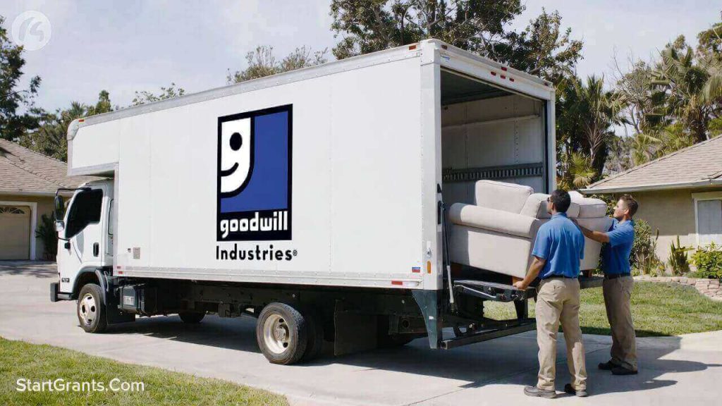 A Goodwill donation pickup truck parked in a residential driveway with drivers loading furniture.