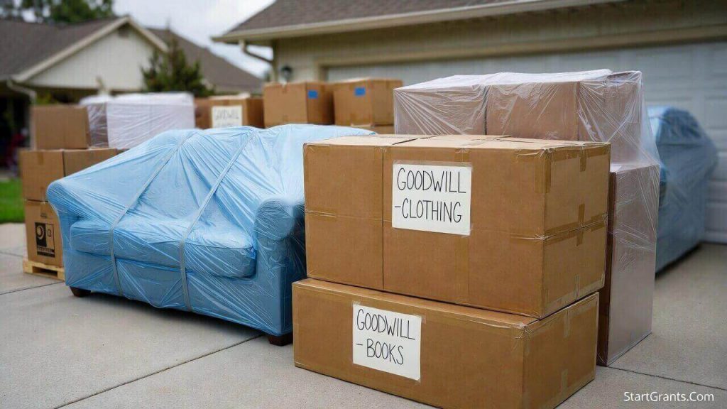 A perfectly organized curbside staging area for a Goodwill donation pickup featuring labeled boxes and a tarp-covered sofa.
