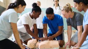 A group of school teachers and coaches practicing CPR and how to use an AED on a medical dummy during a grant-funded safety training session.