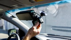 A driver removing a FasTrak toll transponder from their windshield before donating their car to avoid highway fees.