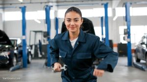 A confident auto mechanic student holding a wrench in a modern training shop