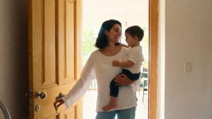 A relieved single mother standing in the doorway of a simple, safe apartment, holding her child’s hand while looking at a set of house keys.