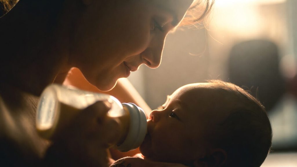 A relieved mother bottle-feeding her newborn baby using free formula obtained from a WIC program.