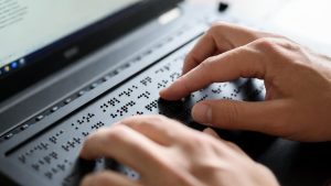 Visually impaired user typing on a refreshable Braille display connected to a laptop.