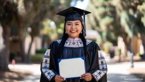 A proud Native American college student holding a diploma and wearing graduation attire with traditional beadwork