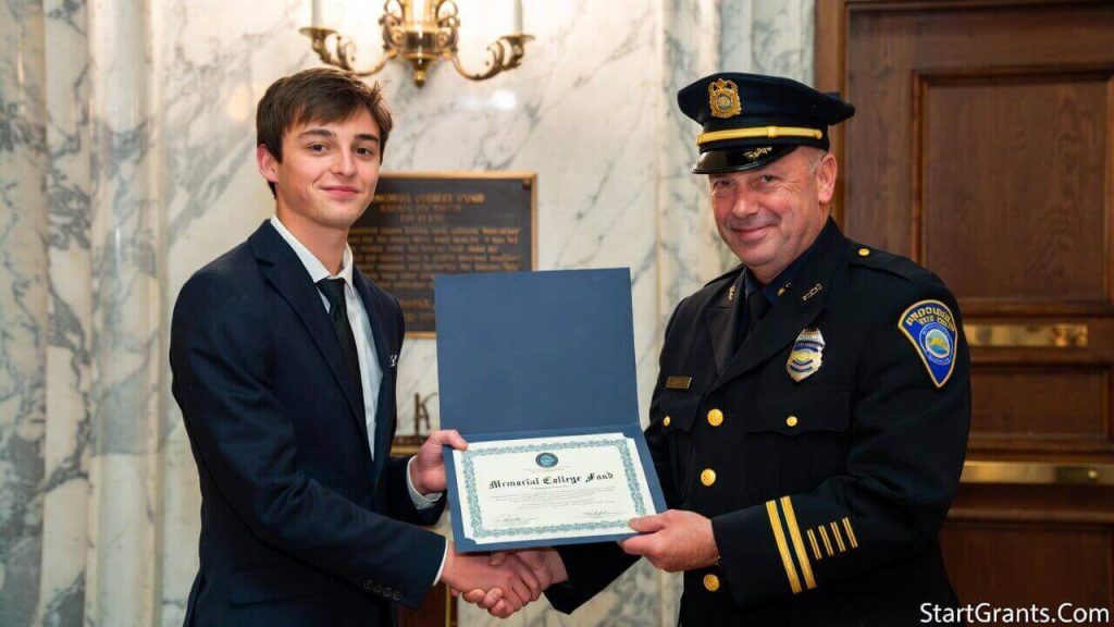 The dependent child of a fallen police officer receiving a memorial college scholarship certificate from a police chief during a formal precinct ceremony.