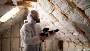 A certified contractor installing blown-in cellulose funded by a government grant for home insulation.