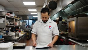 Latino restaurant owner working in commercial kitchen applying for PepsiCo Juntos Crecemos grant