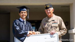 A grandchild of a military veteran receiving a college scholarship check from an American Legion representative.