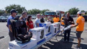 A community safety event where families are receiving free car seats from volunteers at a fire station.