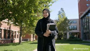 A Muslim college student walking on campus, funded by Riba-free educational grants and VSO scholarships.