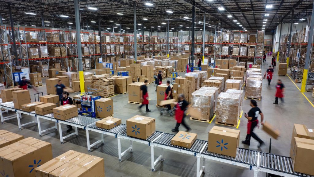 Employees working in a large, busy Walmart warehouse distribution center moving boxes on a conveyor belt.