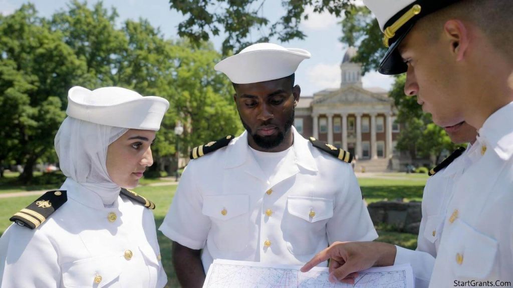 Diverse Navy ROTC midshipmen, including a female in a Hijab and a male with a beard, reviewing charts on a college campus.