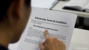 A law student carefully reading the fine print of a conditional scholarship offer outlining the strict GPA requirements tied to the forced 1L curve.
