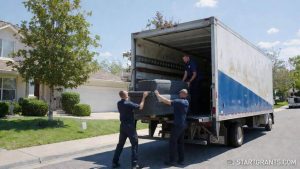 Charity workers loading a heavy sofa into a box truck directly from a residential driveway during a free furniture donation pick-up.