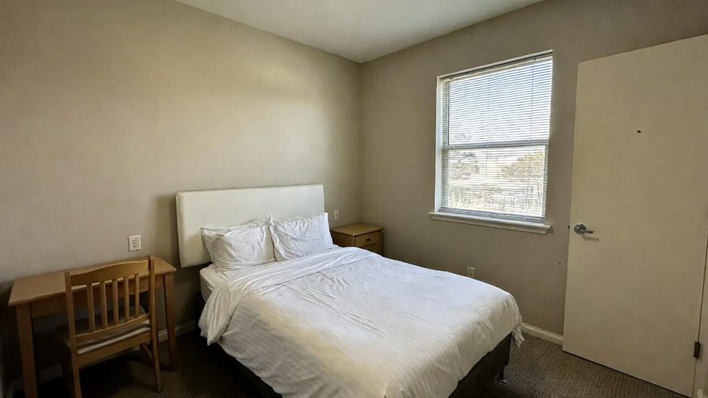 Interior of a clean, private bedroom with a single bed and desk inside a transitional housing unit.