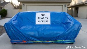 A heavy-duty blue plastic tarp covering an upholstered sofa left in the driveway for a charity donation pick-up to protect it from rain.