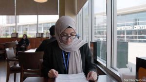 A Muslim graduate student wearing a conference badge reviews a menu at a local restaurant to accommodate Halal dietary restrictions during academic travel.