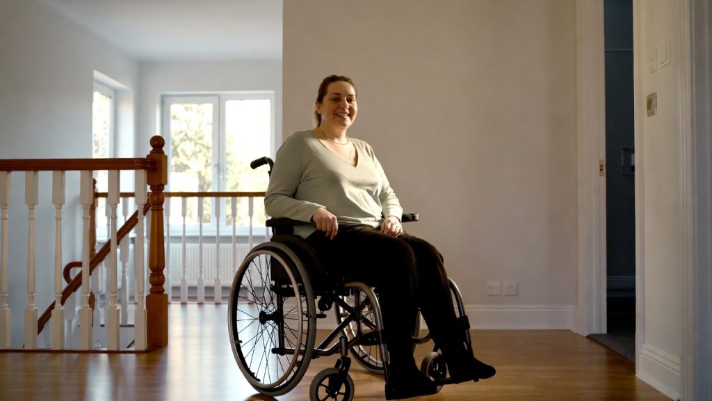 An empowered disabled woman in a wheelchair inside a bright, modern accessible kitchen, representing housing independence in 2026.