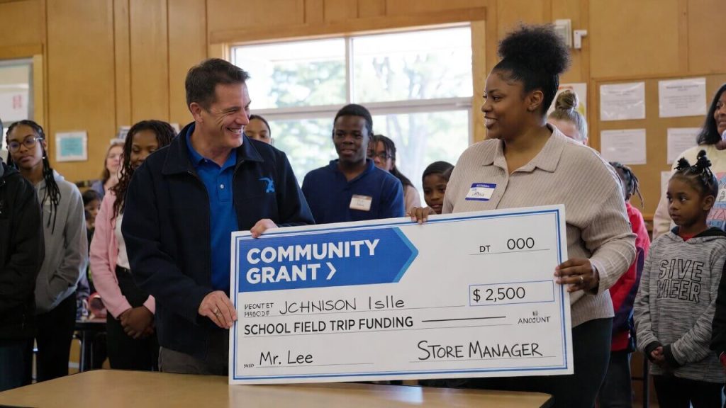 Teacher accepting a community grant check from a local store manager for school field trip funding.