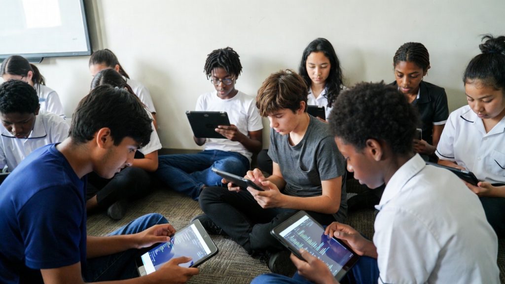 Diverse students sitting on floor using iPads for coding lesson.