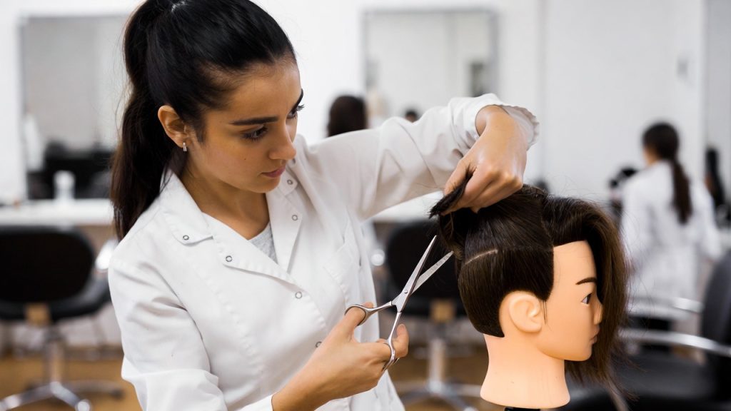 A focused cosmetology student cutting hair on a mannequin head in a bright salon classroom.