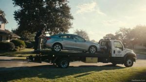 A commercial flatbed tow truck picking up a donated sedan from a residential driveway for charity.