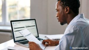 An unemployed adult reviewing job retraining paperwork and grant applications on a laptop, representing WIOA grants for displaced workers.